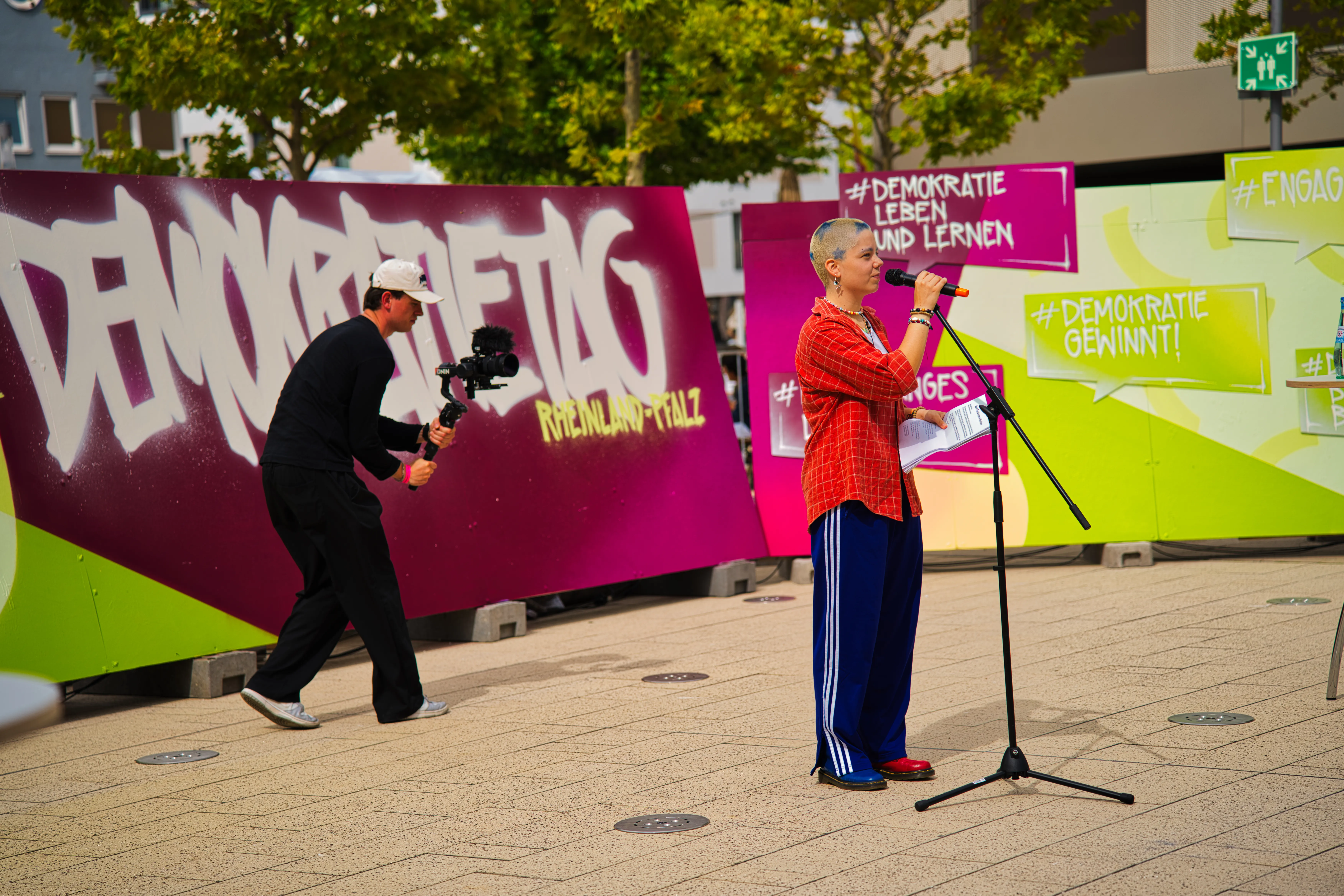 Person am Mikrofon, während sie von einem Menschen mit mobiler Kamera gefilmt wird.